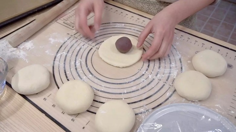 日式红豆包,取一个松弛好的面团，擀成圆形，放入一个豆沙球