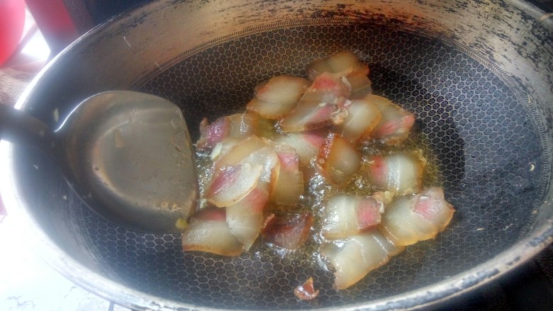 农家干菜油焖春笋,先将腊肉下锅煸炒出油。然后将腊肉扒到锅子一边。