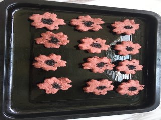 浪漫樱花饼干,将樱花面片逐个移入刷好低油的烤盘中，并在花朵中心位置撒上少许芝麻进行装饰；