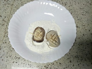 香菇素鲍鱼,然后对折，用牙签从中间穿过，两面蘸上面粉