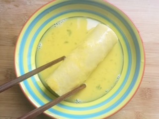 辅食计划十牛油果香蕉卷,将卷好的香蕉卷放入蛋液中，均匀的裹上蛋液。