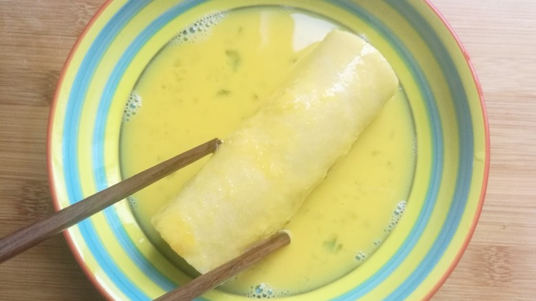 辅食计划十牛油果香蕉卷,将卷好的香蕉卷放入蛋液中，均匀的裹上蛋液。