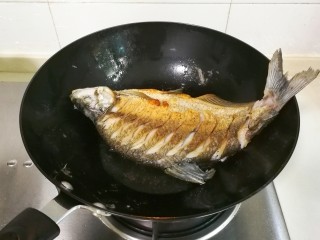 红烧蒜苔鳊鱼,调大火煎十几秒调中火煎，把锅要转动煎鱼的各个部位至煎黄，翻面再这样煎黄