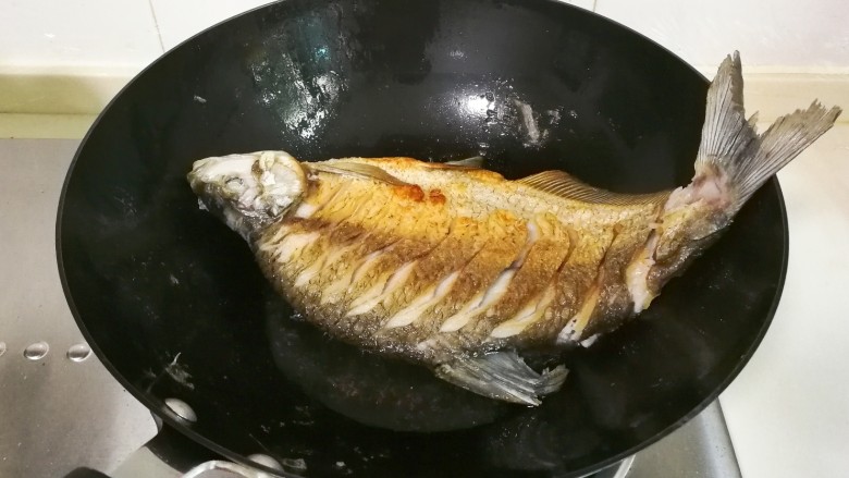 红烧蒜苔鳊鱼,调大火煎十几秒调中火煎，把锅要转动煎鱼的各个部位至煎黄，翻面再这样煎黄