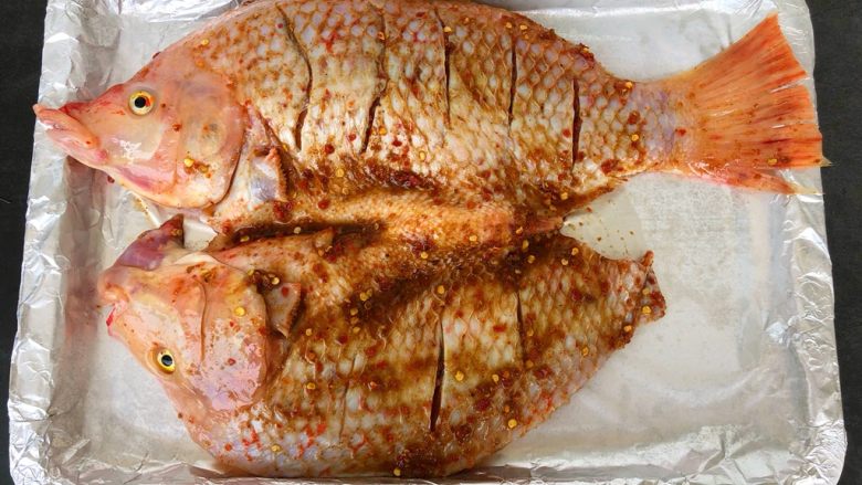 烤箱版烤鱼,烤盘铺上锡纸，在锡纸上均匀的放上20g的姜片和20g的葱白，再放上腌制好的鱼，用刷子在鱼身上均匀的刷上油