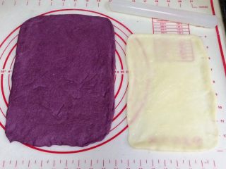 紫薯麻薯夹心软欧,取一份松弛好的面团，用手拍扁，用擀面杖把面团擀开，翻面再擀会，用手整理成长方形，压薄底边。取一份麻薯，继续用擀面杖擀成比面片小点的长方形。
