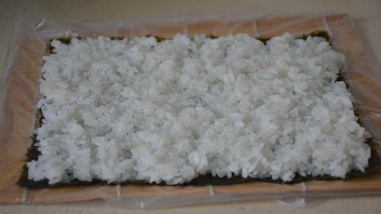 寿司,用手将米饭均匀的平铺在海苔上。用手轻轻压实，将四周多余的米饭摘干净。