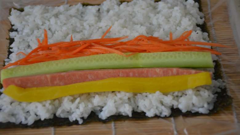 寿司,在靠近自己的一边，依次摆上寿司大根条，黄瓜和火腿条。放适量的胡萝卜丝。