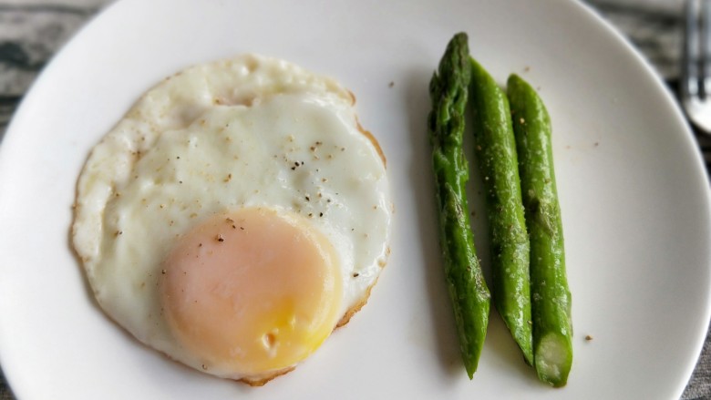 养颜营养早餐,煎好的鸡蛋装入盘子，芦笋装盘撒上胡椒粉