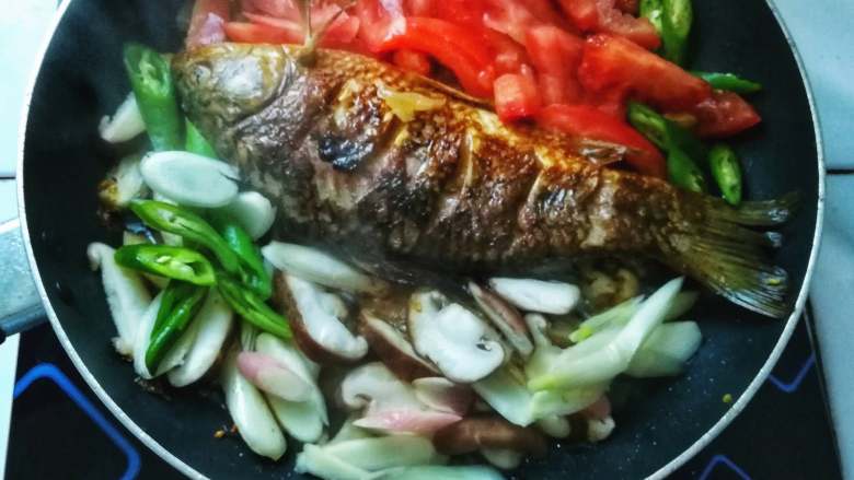 香煎鲫鱼,下香菇、番茄和剩下的青椒至油锅中，不时小心翻炒，以免破坏鲫鱼的完整度；