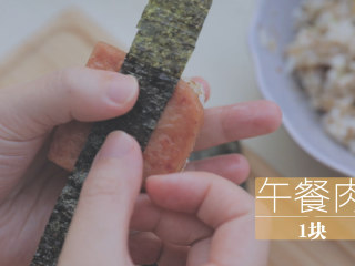 春の饭团的2+1种有爱做法「厨娘物语」,取30g米饭握紧成一个小正方形，放上1块煎好的午餐肉，包入海苔片。
