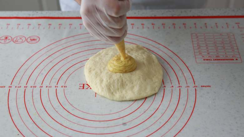爆浆流心面包,取出完成发酵后的面团，用手排气压开，挤入芒果夹心馅料，轻轻包起