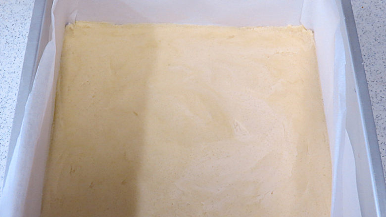 法式小甜点【椰蓉柠檬小方】,将面团放入铺了油纸的烤盘内。用手把面团压平