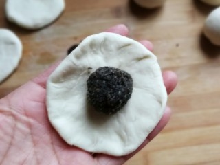 熊猫豆沙馒头,取一份醒发好的面团，用手压成中间厚四周薄的面片，再放上一份豆沙馅儿，包起来然后搓圆