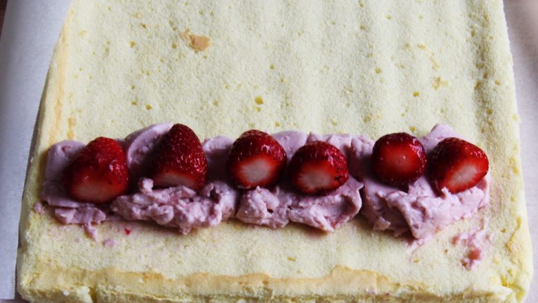 草莓慕斯蛋糕卷,冰箱中拿出凝固的草莓慕斯糊放在蛋糕体三分之一处，6粒草莓排立整齐。