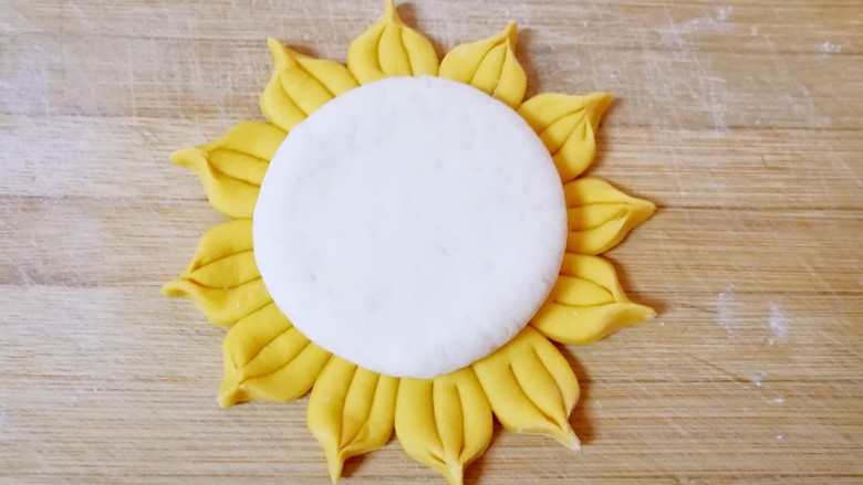 向日葵馒头,取一个白色的小剂子擀成小一点的圆饼状，放在做好的向日葵中间。