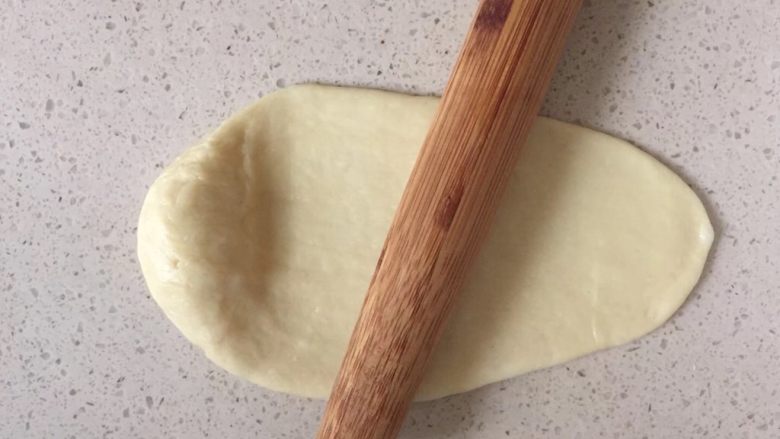 【一口接一口系列】肉松面包&椰蓉面包,取一个小面团，用擀面杖将面团擀成椭圆型，顶部留少许不擀，底部擀成薄片