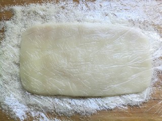 椰蓉豆沙糯米卷,把糯米团没盖保鲜膜的一面朝下放到案板上。