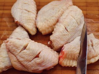 三汁焖鸡翅,把鸡翅冲洗干净后，放到菜板上，用刀把鸡翅正面和反面都划两刀，这样做的目的是为了腌制鸡翅的时候，鸡翅能入味