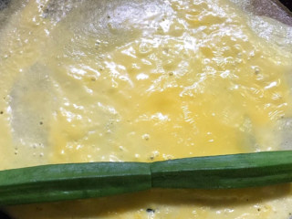 秋葵厚蛋烧,蛋液还没有完全煎熟，上面还有一点粘的时候，把两根秋葵排成一条直线放入蛋饼中。