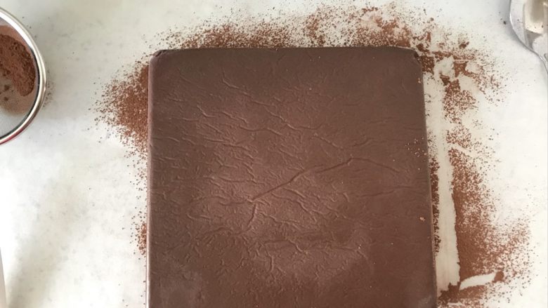 生巧,台面上铺上油纸，晒一些可可粉，把冷冻好的巧克力取出，撕掉油纸，倒扣在撒好可可粉的油纸上。