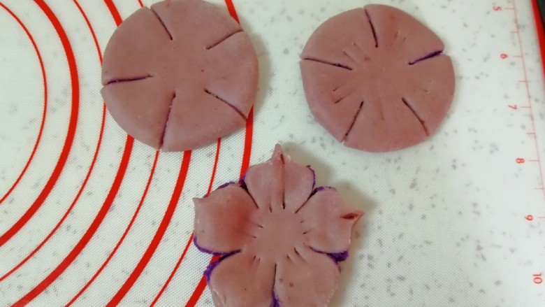 紫薯桃花酥,包好的面团压扁擀平，用刮刀切成5瓣，中间不要切断，每瓣的中间再用刮刀压两道，末端用大拇指和食指捏出桃花的花瓣。