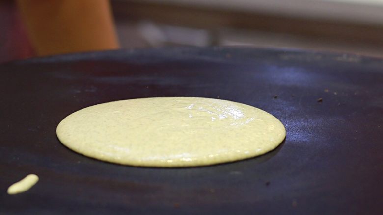 美味早餐 妈妈味道的绿豆煎饼果子,饼铛烧热后改小火，在饼铛上滴两滴的油，并用厨房用纸将油抹均匀。用汤勺舀起一勺面糊倒在饼铛上。
