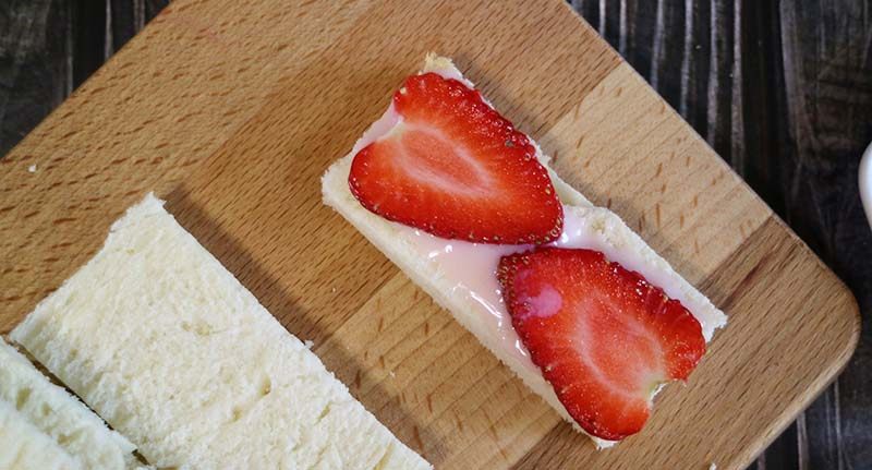 美味早餐缤纷水果三明治,将<a style='color:red;display:inline-block;' href='/shicai/ 893'>炼乳</a>用小勺子或者抹刀将抹在切好的吐司上，再放上一层草莓片。