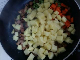 腊肉土豆焖饭,倒入土豆，胡萝卜和豌豆，翻炒均匀。