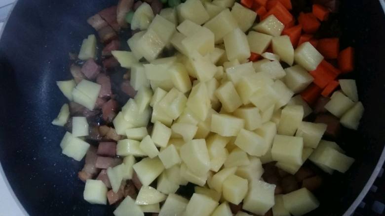 腊肉土豆焖饭,倒入土豆，胡萝卜和豌豆，翻炒均匀。