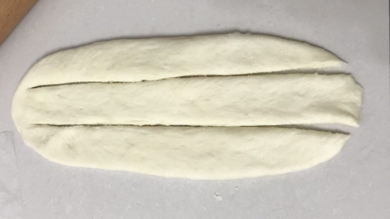 椰蓉排包,取一个面团用手按压再擀成长舌形，用括板切成三条，一头不要切断。编辫子那样编好。