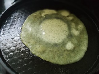 艾叶鸡蛋卷饼,倒入一勺艾叶面糊，摊成厚薄适中的圆形，煎成面饼