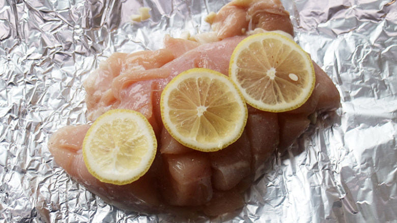 美味又减脂的缤纷鸡胸沙拉,鸡胸肉放在锡纸上，肉的表面放柠檬片。