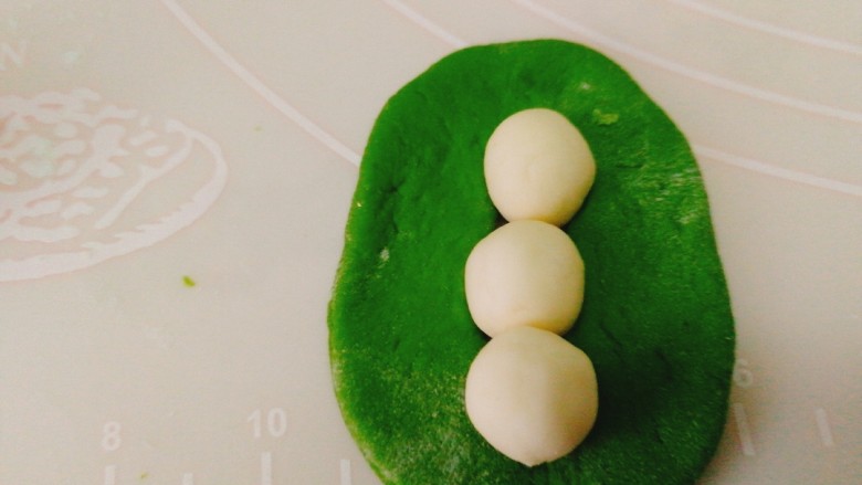 人见人爱的豌豆荚馒头,取出少量白色面团，搓小圆后放在绿色面团中间