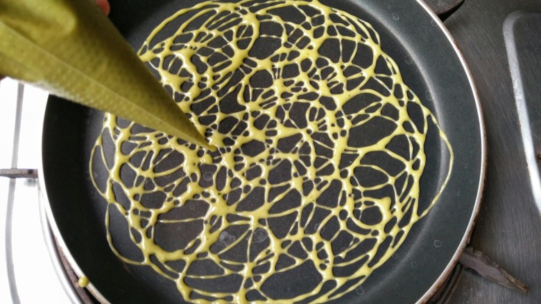 蕾丝蛋卷――高颜值的下午茶小点,将不粘平底锅预热后，用裱花袋将蛋粉糊画圈均匀挤入锅中。