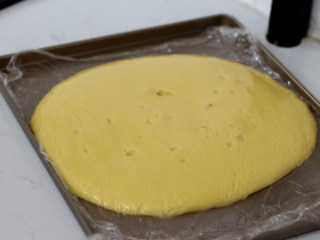 低脂豆乳天使蛋糕卷,倒入不粘烤盘中，摊开后，保鲜膜贴面保存放凉备用。