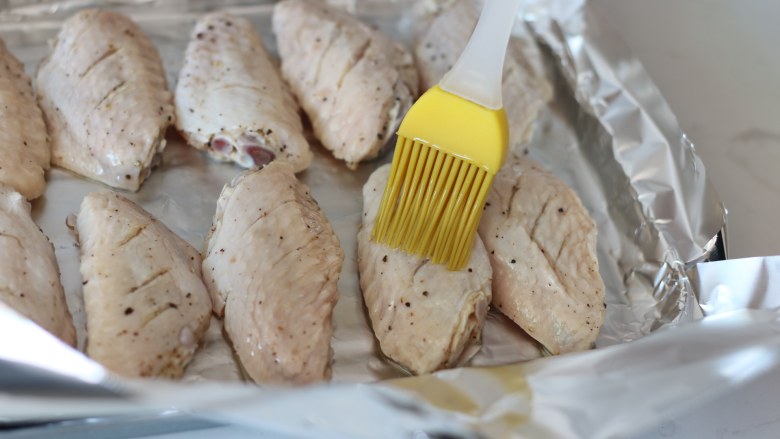 柠檬黑胡椒烤鸡翅,腌制好的鸡翅中摆放在烤盘上，在表面再薄薄刷一层油。九阳的这款12L烤箱自带的烤盘摆放12个翅中刚刚好