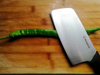 辣椒炒肉丝,取一个线椒放在案板上，用刀背一拍。