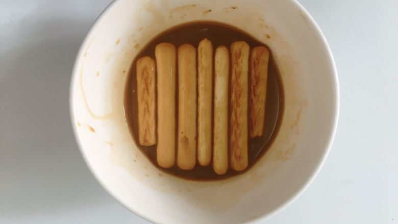 提拉米苏,将手指饼放入朗姆酒和浓缩咖啡混合好的液体蘸一层，铺在容器的底部。