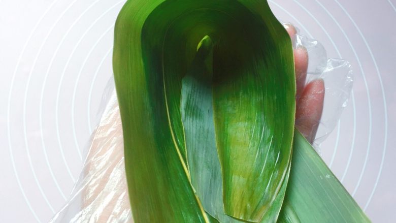 花生蜜枣粽,在粽叶的1/3处折起，折出一个漏斗形状（漏斗下方一定要紧密，不然会漏米）；
