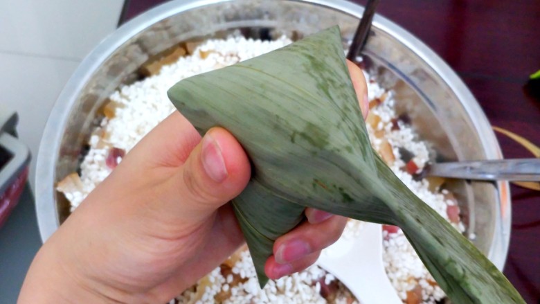 不同类型粽子的包法,把长叶子往下压，拇指和食指把两边叶子固定住。