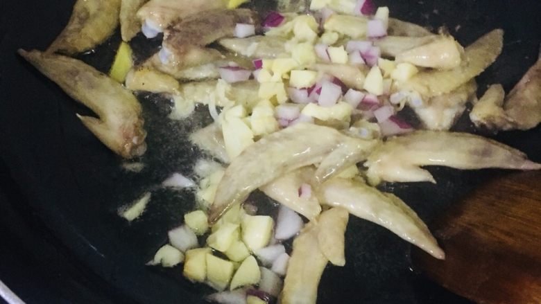 蒜香鸡翅尖,倒入蒜末和洋葱翻炒