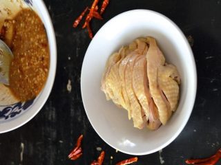 口水鸡,水烧开加姜和葱。加入鸡肉，煮熟。将鸡肉从锅中取出，放入冰块中，让鸡肉完全冷却。鸡肉切成薄片，放在碗里。