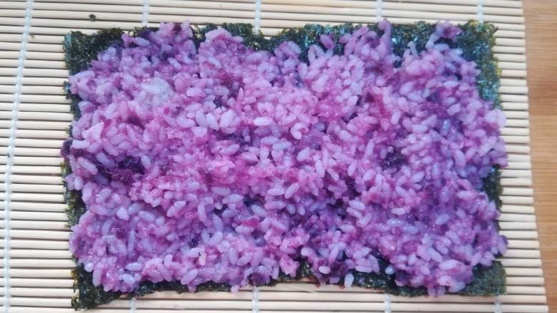 紫薯寿司,把拌匀的紫薯米饭均匀的铺在紫菜上，紫菜的两端也要有米饭粒。如果觉得米饭比较粘，可以用勺子沾水，有勺背来把米饭推均匀。用手来操作的话，也可以在手上抹些凉开水，或寿司醋防止黏手。