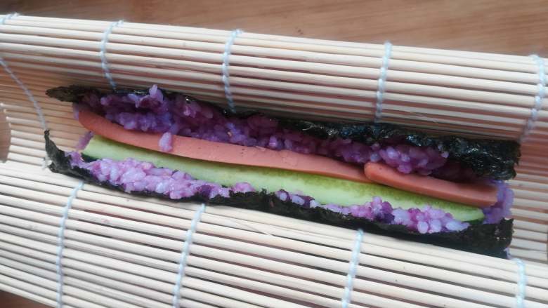 紫薯寿司,用手托起卷帘，让两端粘合在一起。因为米饭有粘性，会很自然的粘合在一起。