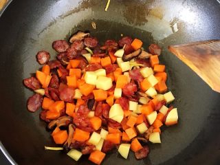 腊肠土豆焖饭,等腊肠微微出油变透明后加入胡萝卜和土豆丁，继续翻炒，直到胡萝卜土豆断生。加入少许盐和老抽调味