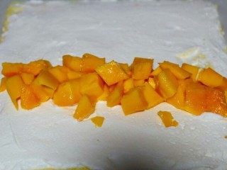 芒果蛋糕卷,在奶油表面摆放一排切好的芒果果肉


