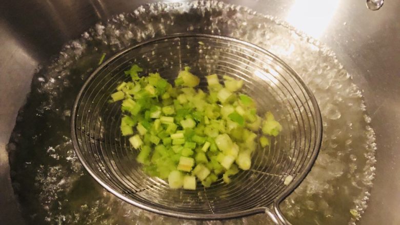 凉拌芹菜毛豆米,将芹菜粒放抄网里在热水里烫10秒钟，拿出，直接沥干水倒入调料碗里。