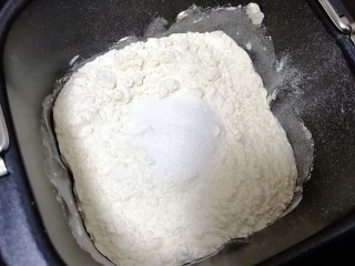 南瓜油渣包, 混合好的南瓜泥倒入面包机桶内，加入面粉和糖，启动面包机的和面程序10分钟(没有面包机用手和面是一样的)。