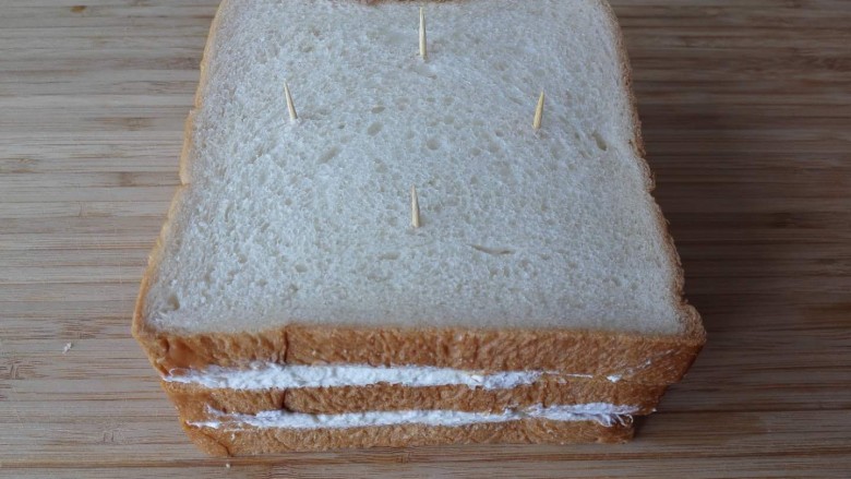 芒果淡奶三明治—夏日里的清凉快手早餐,涂上两层奶油后盖上第三片面包，用牙签固定三明治，这样切的时候不会走样。